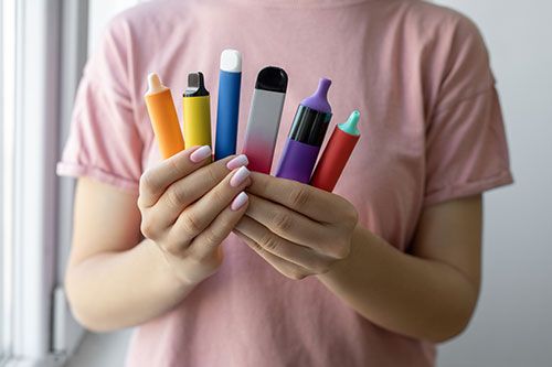 A person holding six different e-cigarettes