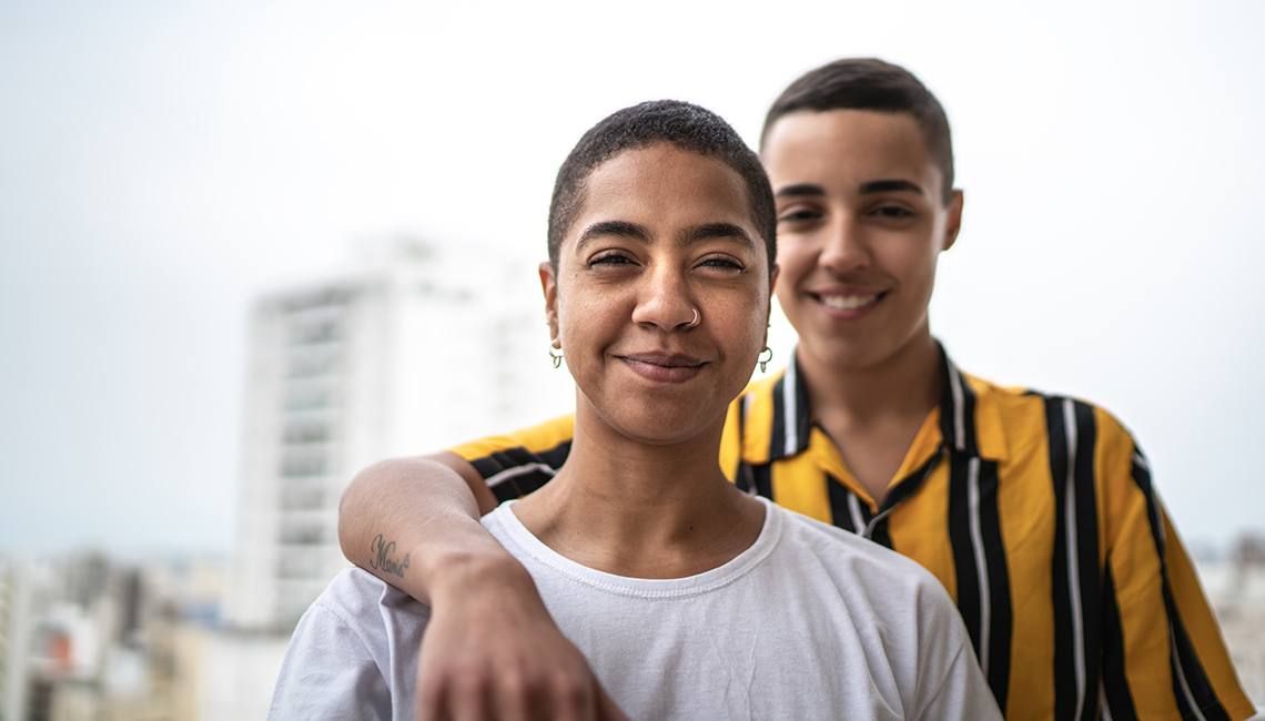 two gender non-conforming people looking at the camera and smiling