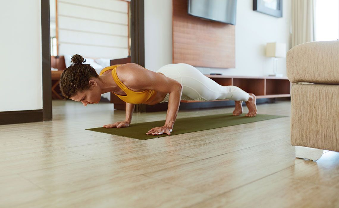 A woman performing push-ups on an exercise mat at home