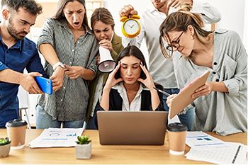 Someone sitting at desk with people representing stressors surrounding her