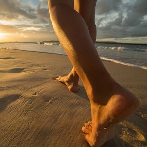 Ankle-down viefw of legs walking on a beach at sunset