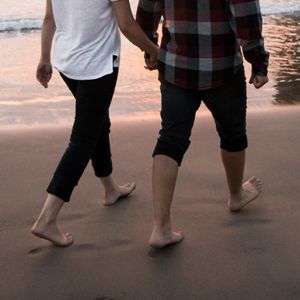 A couple walking barefoot together on a beach at sunset
