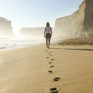 Person walking on a beach with foot imprints in the sand behind them